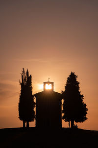 Silhouette of a chapel with trees against sky during sunset