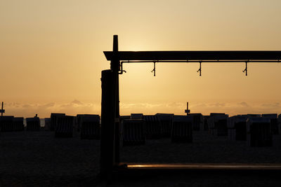 Silhouette wooden posts in sea against sky during sunset