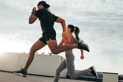 Low angle view of young woman jumping against sky