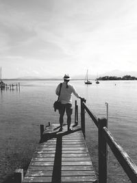 Rear view of man standing on pier at sea against sky