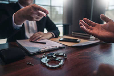 Midsection of man pointing at businessman sitting at table