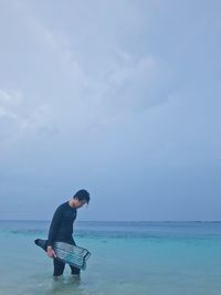 Man carrying diving flippers while walking in sea against sky