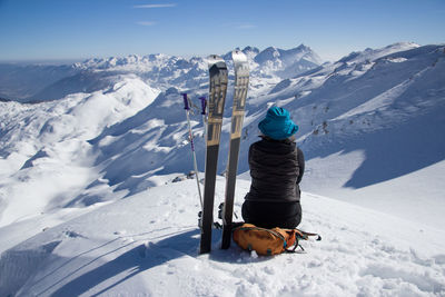 Woman with snowboards sitting on snowcapped mountain against sky