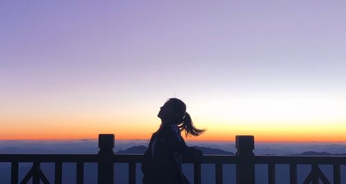 Silhouette woman standing by railing against sky during sunset