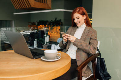 Young woman using mobile phone while sitting on table