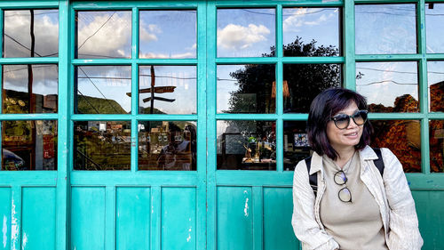 Portrait of smiling young woman standing against window