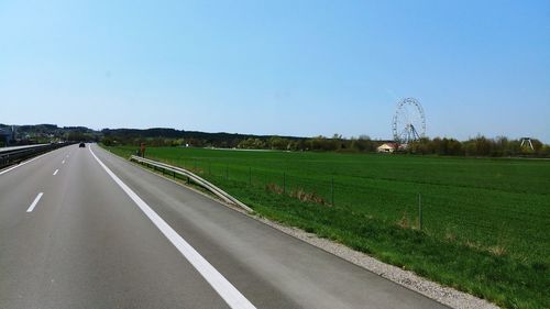 Road amidst field against clear sky