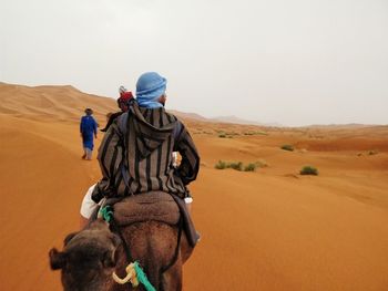 Man riding camel on desert against sky