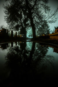 Silhouette trees by lake against sky at dusk