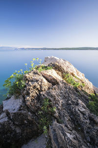 Rocks by sea against clear sky