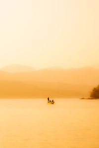 Silhouette people in sea against orange sky