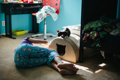 Kitten atop a cat house looks down at girl laying below