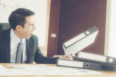 Businessman holding file while yawning at desk in office