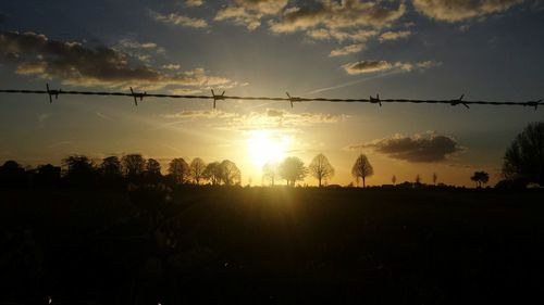 Barbed wire on silhouette landscape against sunset