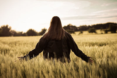 Rear view of woman on field against sky during sunset