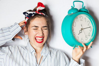 Portrait of screaming woman holding alarm clock against wall