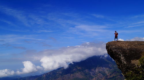 Man standing on rock by mountains against sky