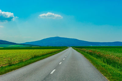 Empty road amidst field against sky