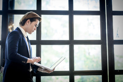 Young woman using mobile phone at window