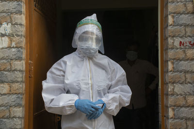 Portrait of woman wearing protective suit standing against wall