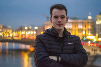 Portrait of young man standing against illuminated city at night