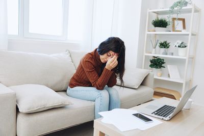 Side view of woman using laptop while sitting on sofa at home