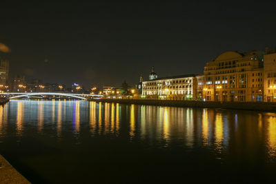 Illuminated buildings by river against sky at night