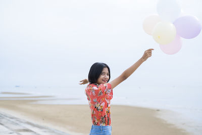 Full length of woman with balloons at beach against sky