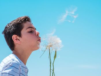 Boy blowing dandelion against blue sky