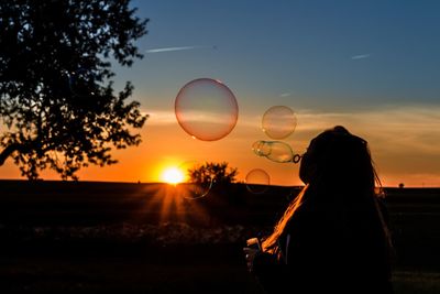 Silhouette woman standing by tree against sky during sunset