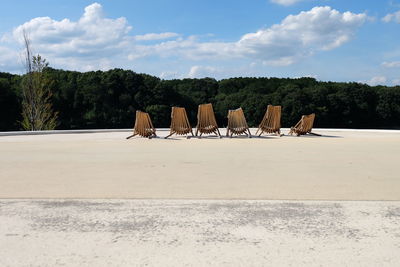 Chairs on road by trees against sky