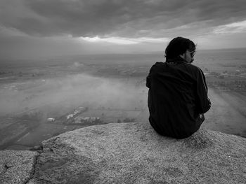 Rear view of man sitting on landscape against sky