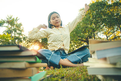 Low angle view of young woman sitting against trees