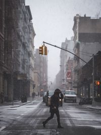 Full length side view of person crossing city street during snowfall