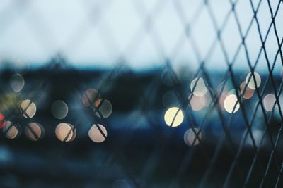 Defocused lights seen through chainlink fence at dusk