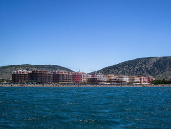 Scenic view of sea and buildings against clear blue sky