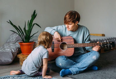 Little girl plays the guitar with her mother on the floor at home