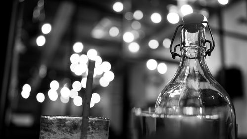 Close-up of bottle by glass in illuminated cafe