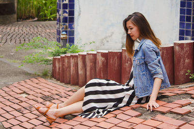 Young woman looking away while standing on footpath