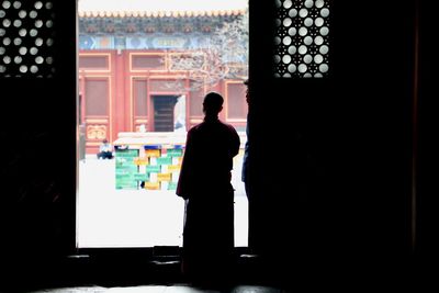 Rear view of silhouette man looking through window in building