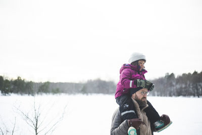 Mature man carrying daughter on shoulders during winter