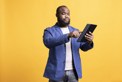 Young man using mobile phone while standing against blue background