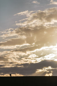 Silhouette of field against cloudy sky