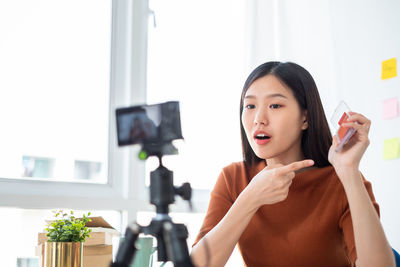 Portrait of young woman holding camera at home