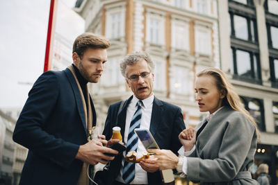 Low angle view of business professionals looking at smart phone while standing in city