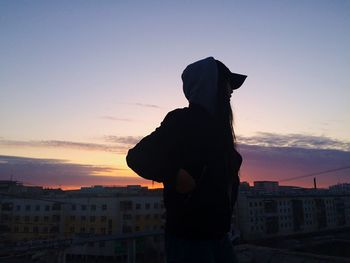 Silhouette woman standing by city against sky during sunset