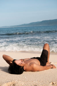 Midsection of man lying on sand at beach of banana island against sky