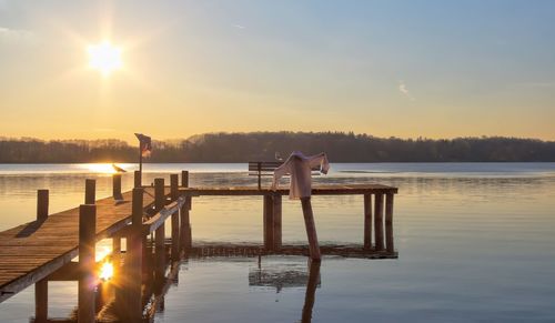 Wooden posts on pier at lake against sky during sunset