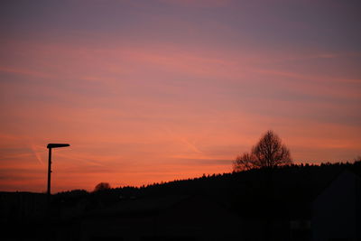 Silhouette trees by street against sky during sunset