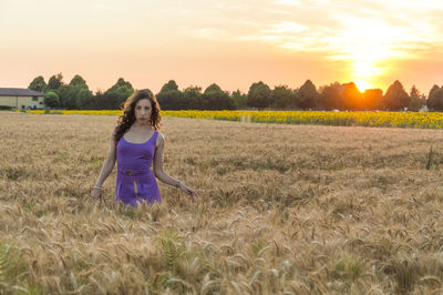 Full length portrait of woman standing in farm against sky during sunset